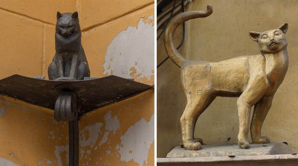 Два бронзовых памятника: сидящий серый кот Елисей и стоящая золотистая кошка Василиса на фоне желтой стены