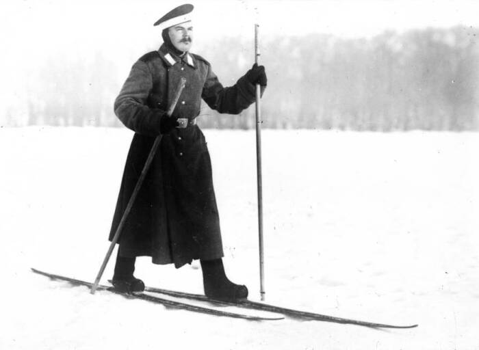 Солдат на лыжах в военной форме и валенках с лыжными палками в зимнем лесу конца XIX века
