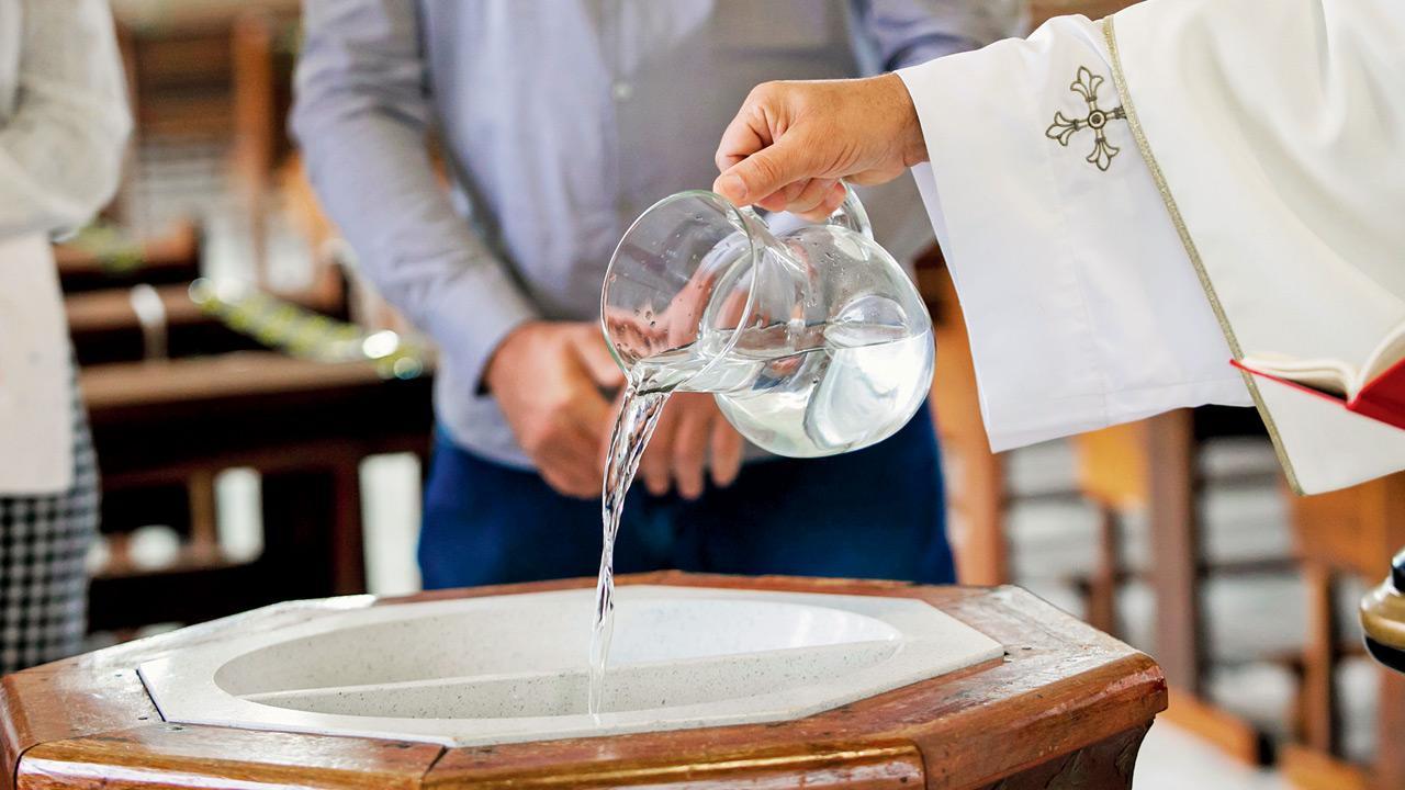 Священник в облачении наливает освященную воду из кувшина в купель во время таинства крещения