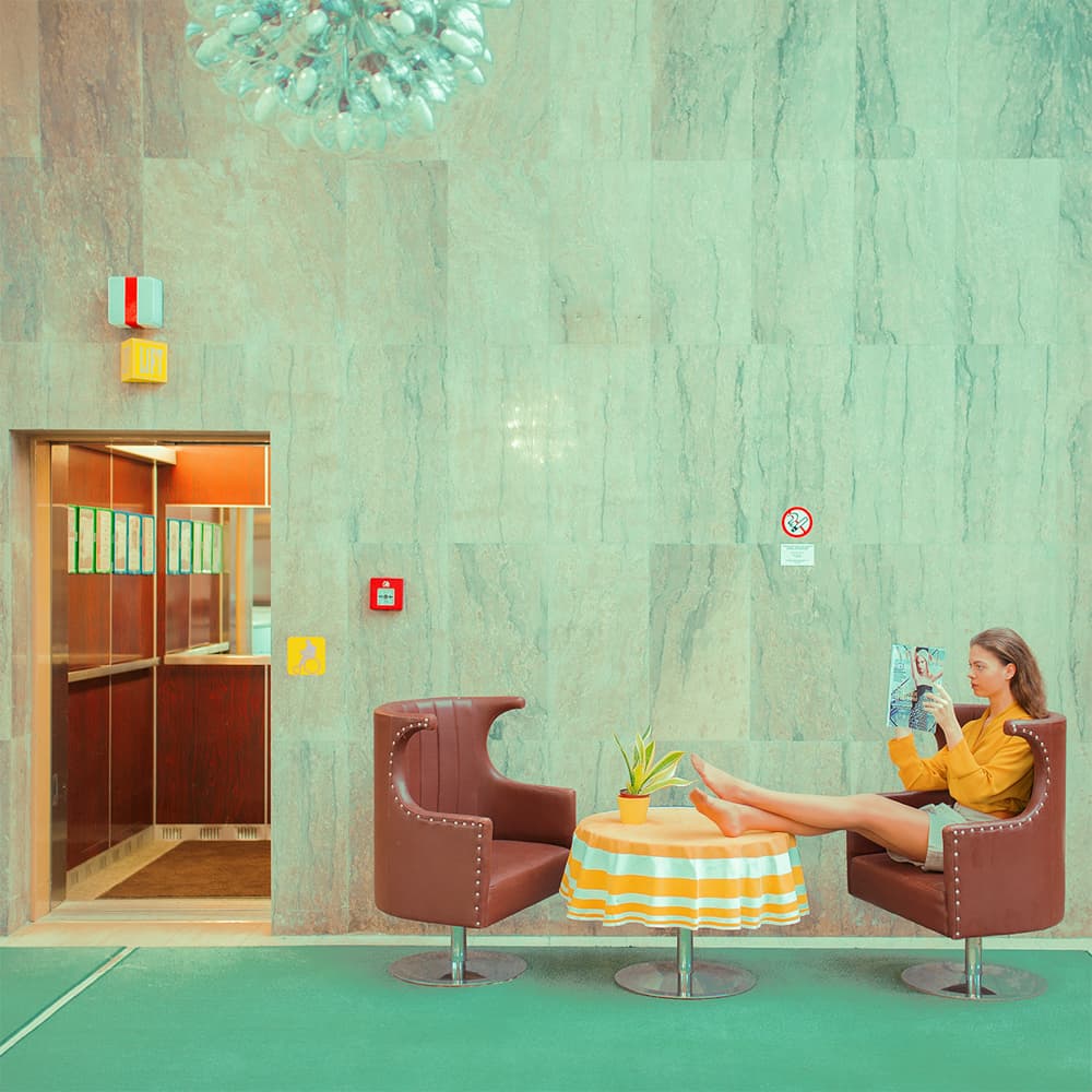 Женщина в оранжевом платье читает журнал, сидя в холле с мраморными стенами