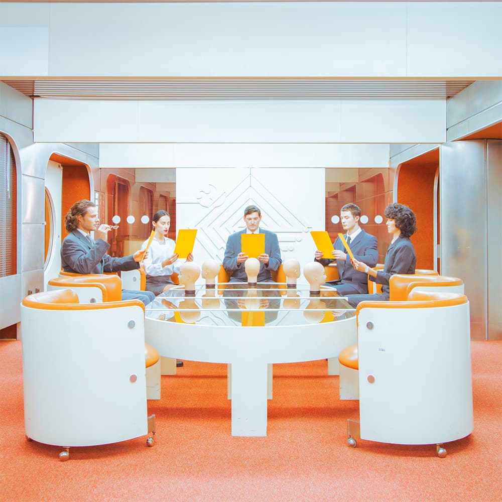 Трое людей в деловых костюмах сидят за круглым столом с манекенами голов в футуристическом офисе 