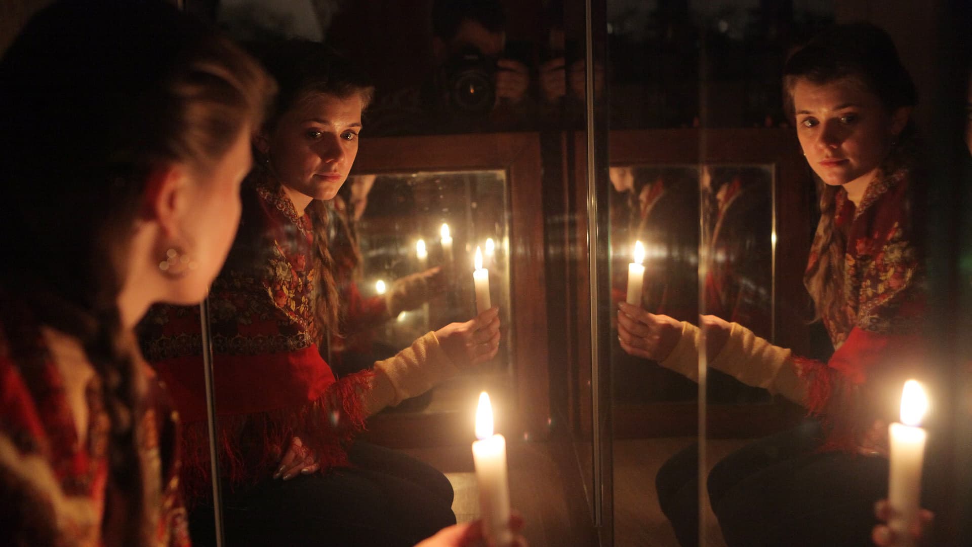 Девушка в традиционной одежде гадает на суженого с зеркалами и свечами