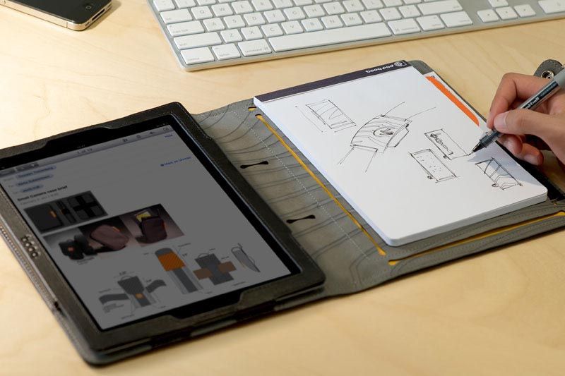 Человек пишет ручкой в блокноте, рядом лежит планшет