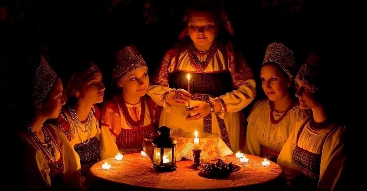 Группа девушек в традиционных русских костюмах за святочным гаданием при свечах