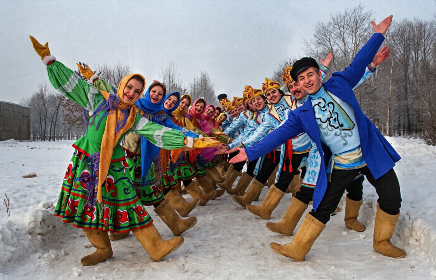Группа людей в народных костюмах и традиционных валенках танцует хоровод на снегу в зимнем русском пейзаже