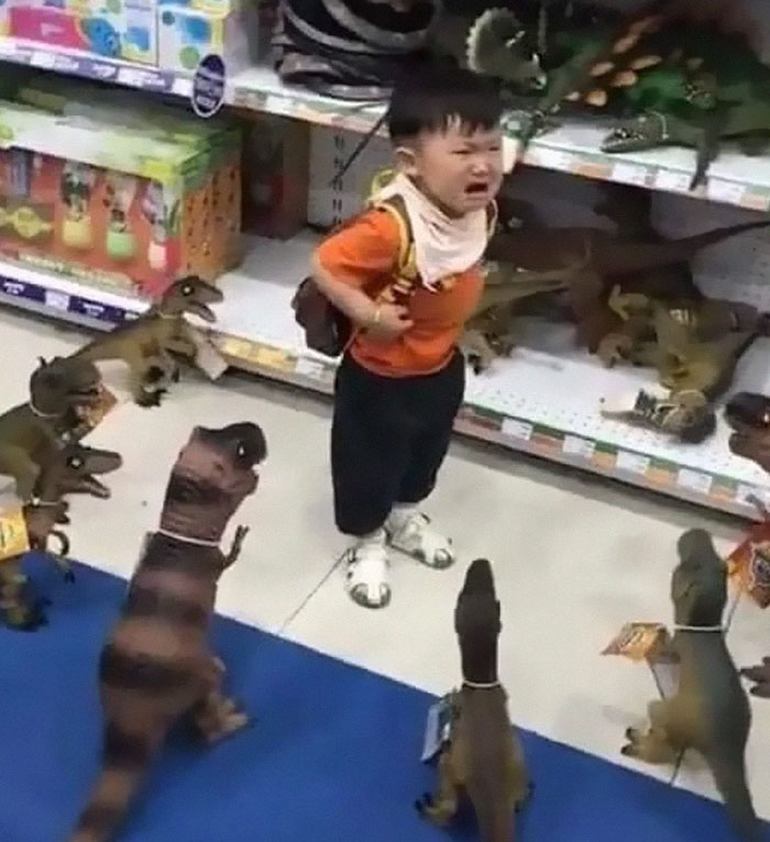 Маленький мальчик плачет в окружении игрушек-динозавров в магазине