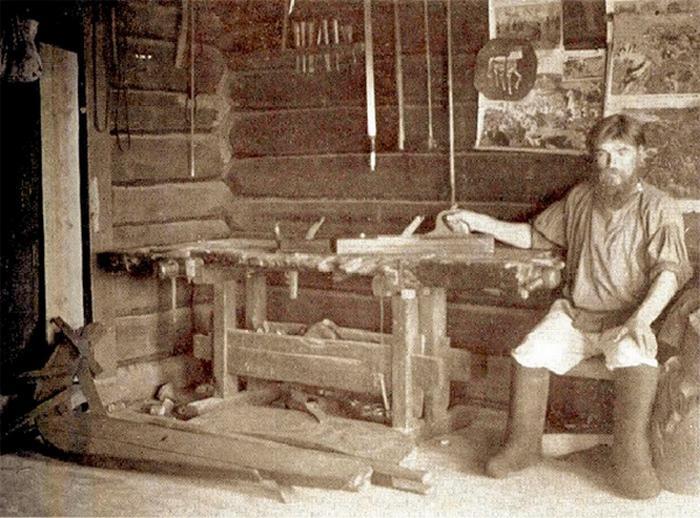 Портрет мужчины в традиционной одежде и высоких серых валенках в интерьере русской избы