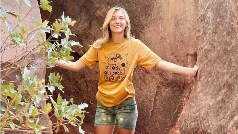 Габби Петито стоит в полный рост на красных скалах в национальном парке Зайон в жёлтой футболке