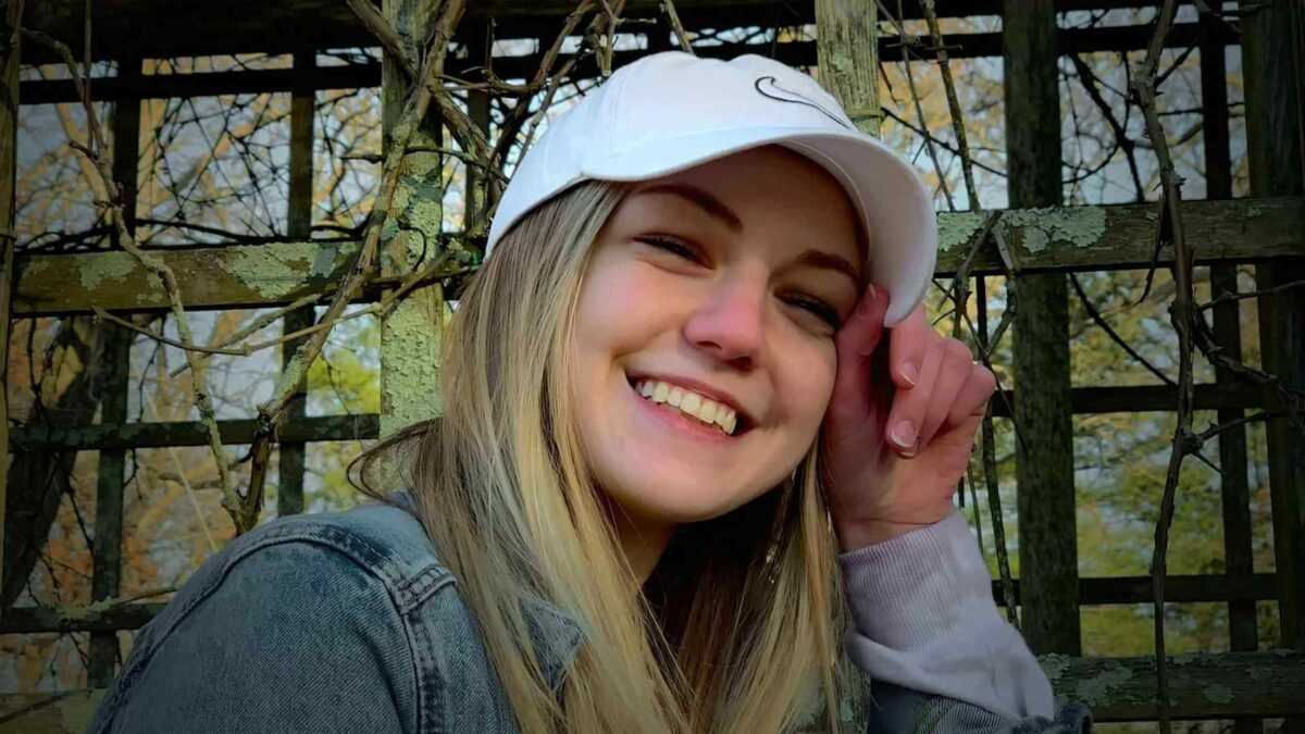 Портрет Габби Петито с улыбкой в белой кепке на фоне зелени