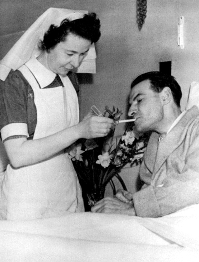 Медсестра в униформе подносит зажженную сигарету лежачему пациенту