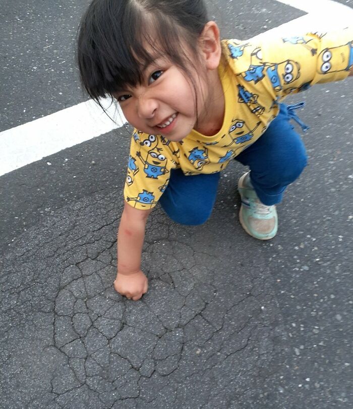 Девочка показывает кулак на асфальте и улыбается в камеру