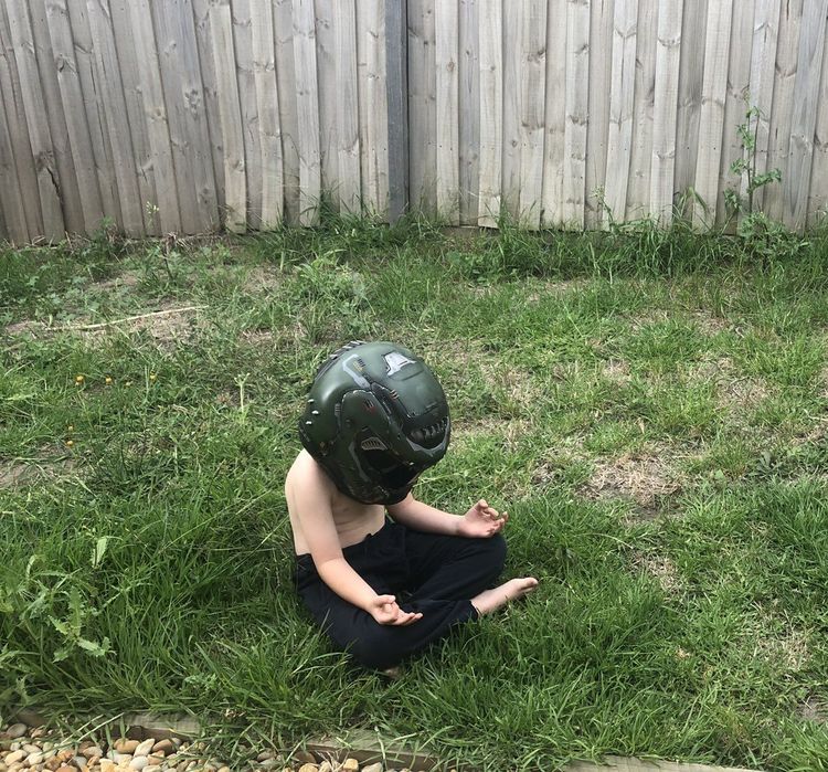 Ребёнок в боксёрском шлеме сидит в позе лотоса во дворе