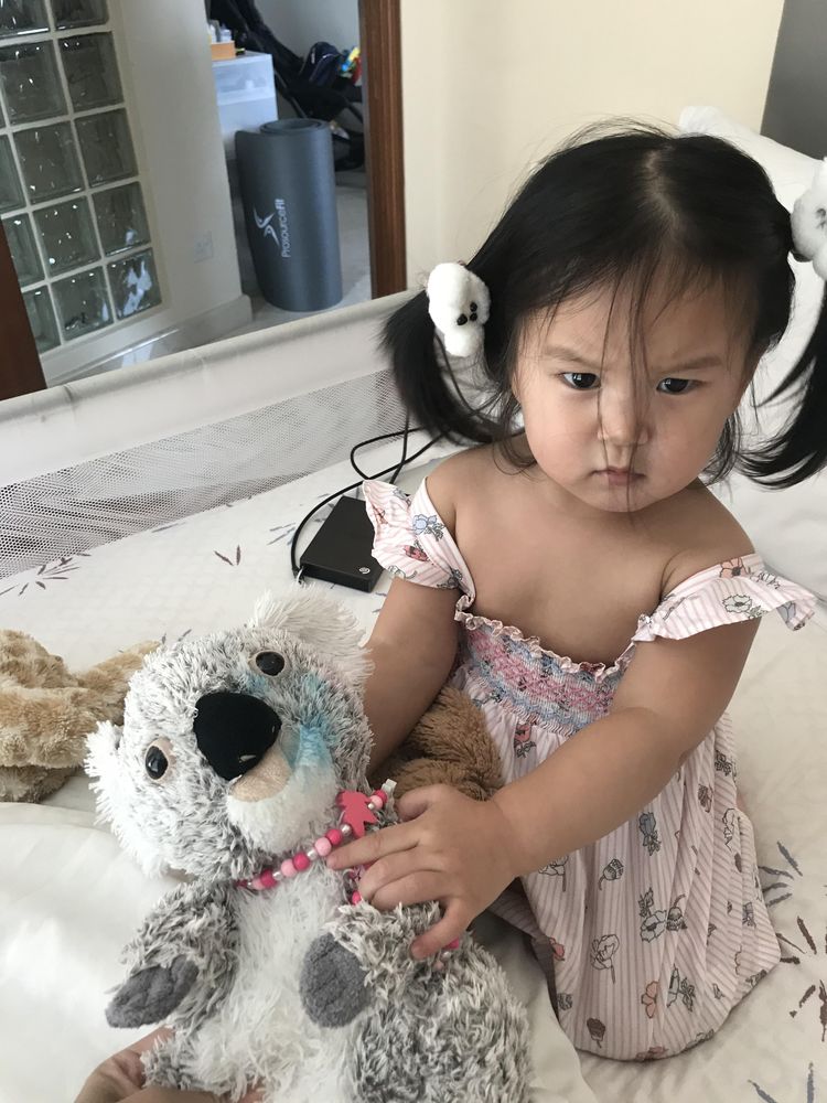 Девочка держит мягкую игрушку коалу с синими пятнами от теней