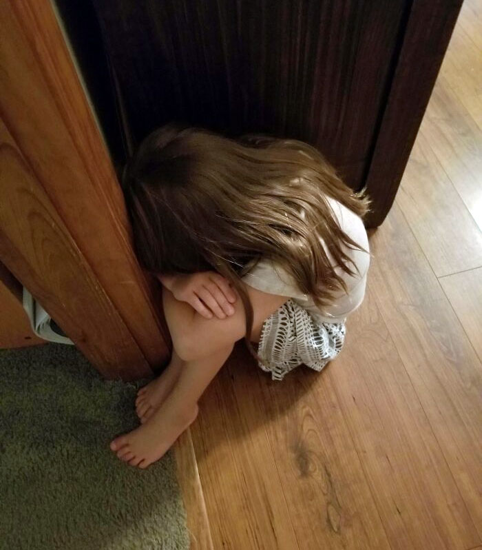 Девочка плачет, уткнувшись в угол двери