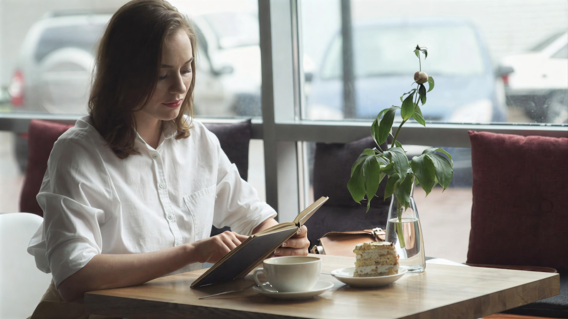 Девушка читает бумажную книгу в кафе без телефона на столе