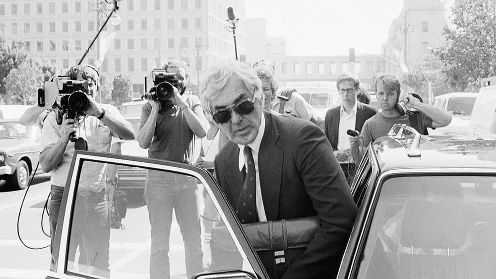 Джон Делореан выходит из автомобиля в окружении журналистов 1982