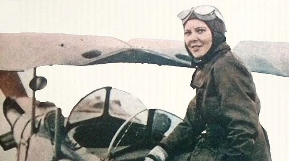 Сабиха Гёкчен в летном шлеме и очках за штурвалом самолета, улыбается в кабине истребителя