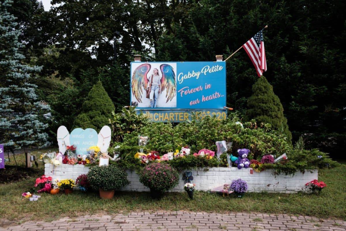 Мемориал Габби Петито с цветами, плюшевыми игрушками, плакатами и крыльями ангела у дерева