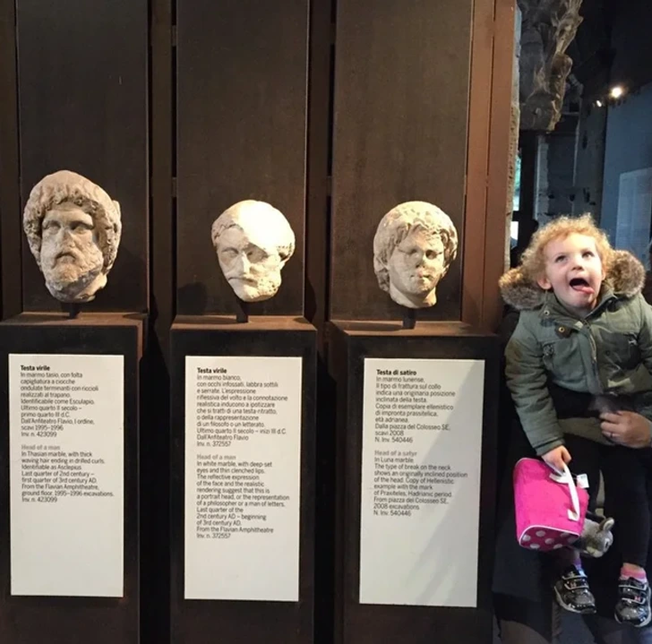 Девочка корчит рожи рядом с античными экспонатами в музее