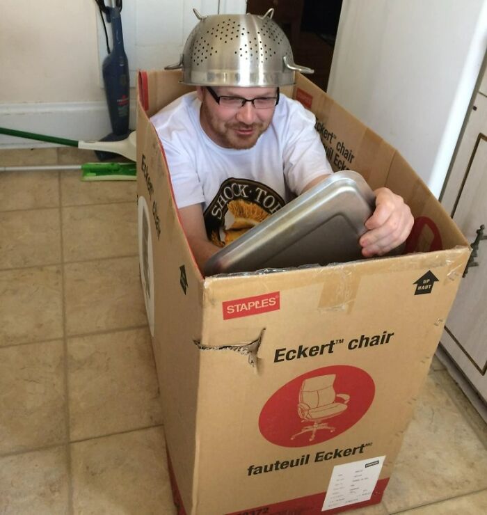 Мужчина в очках сидит в картонной коробке с дуршлагом на голове