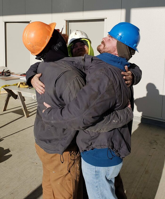 Трое мужчин в строительных касках крепко обнимаются на улице