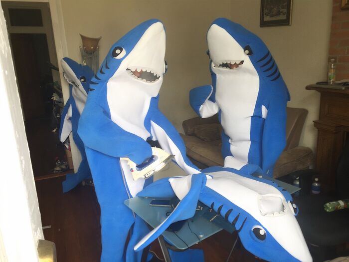 Два человека в костюмах акул гладят третий костюм