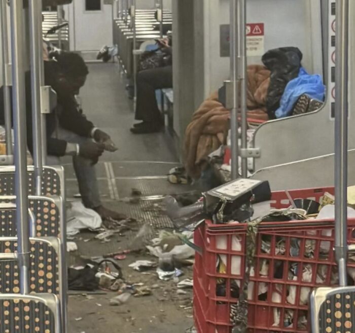 Захламлённый вагон метро с мусором на полу и спящими людьми