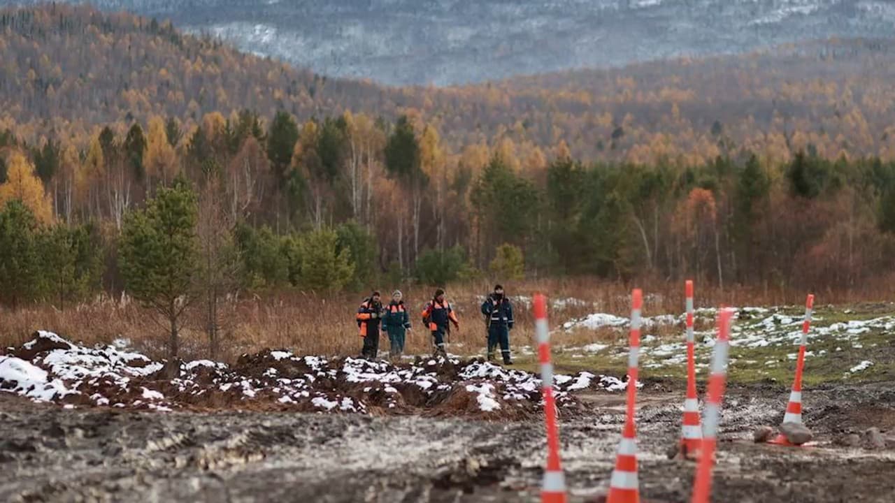 Группа волонтёров в ярких жилетах движется цепочкой по заснеженной горной тропе среди голых деревьев