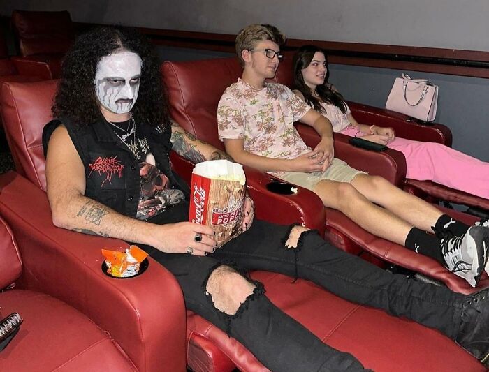 Мужчина с белым гримом на лице держит ведро попкорна в кинотеатре