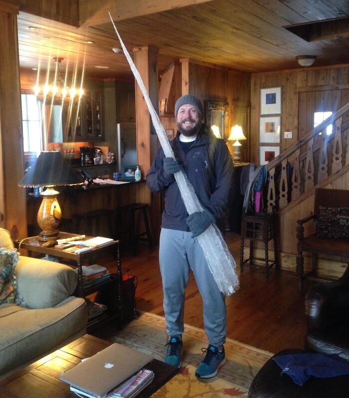 Улыбающийся мужчина в шапке держит огромную длинную сосульку в доме