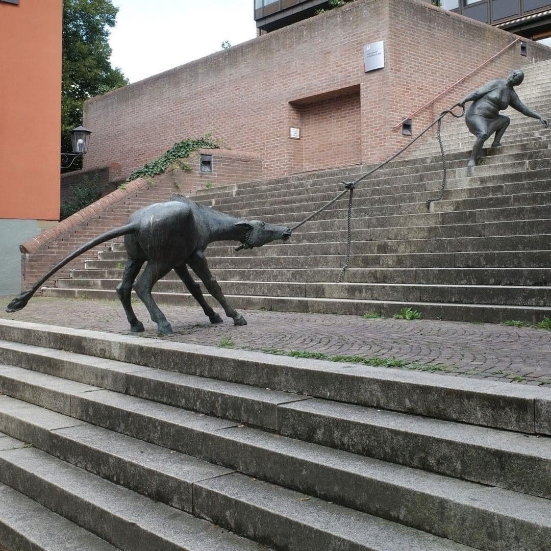 Бронзовая скульптура женщины, тянущей упрямого быка вверх по лестнице