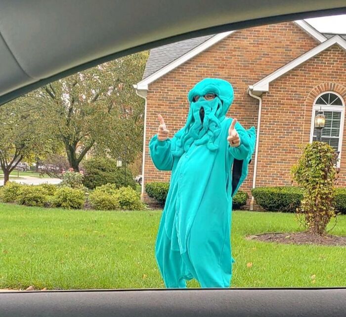 Человек в бирюзовом костюме Ктулху показывает большие пальцы на газоне