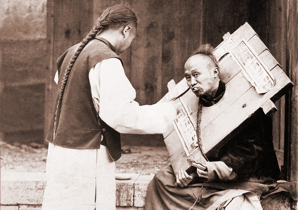 Прохожий кормит с ложки узника в колодке, иллюстрация к описанию беспомощности человека в канге.