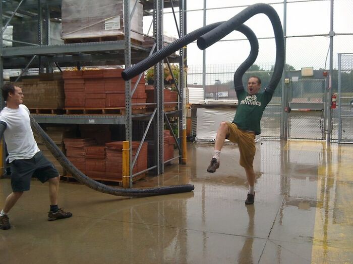 Мужчина прыгает с большой чёрной гофрированной трубой на складе