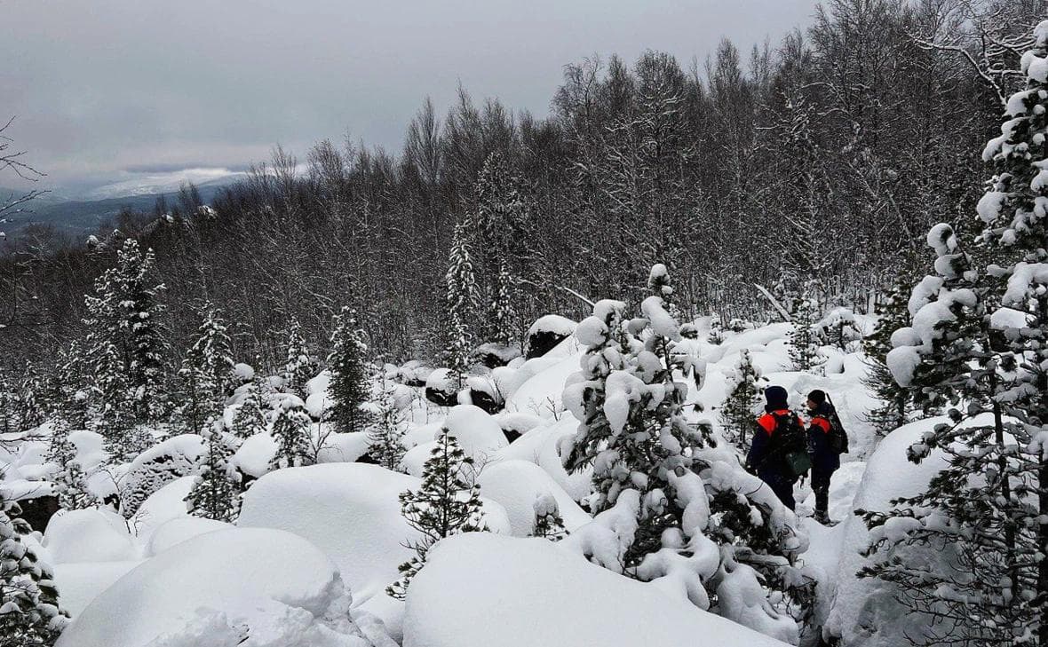Двое спасателей в оранжевых куртках осторожно перебираются по огромным обледенелым валунам, покрытым снегом