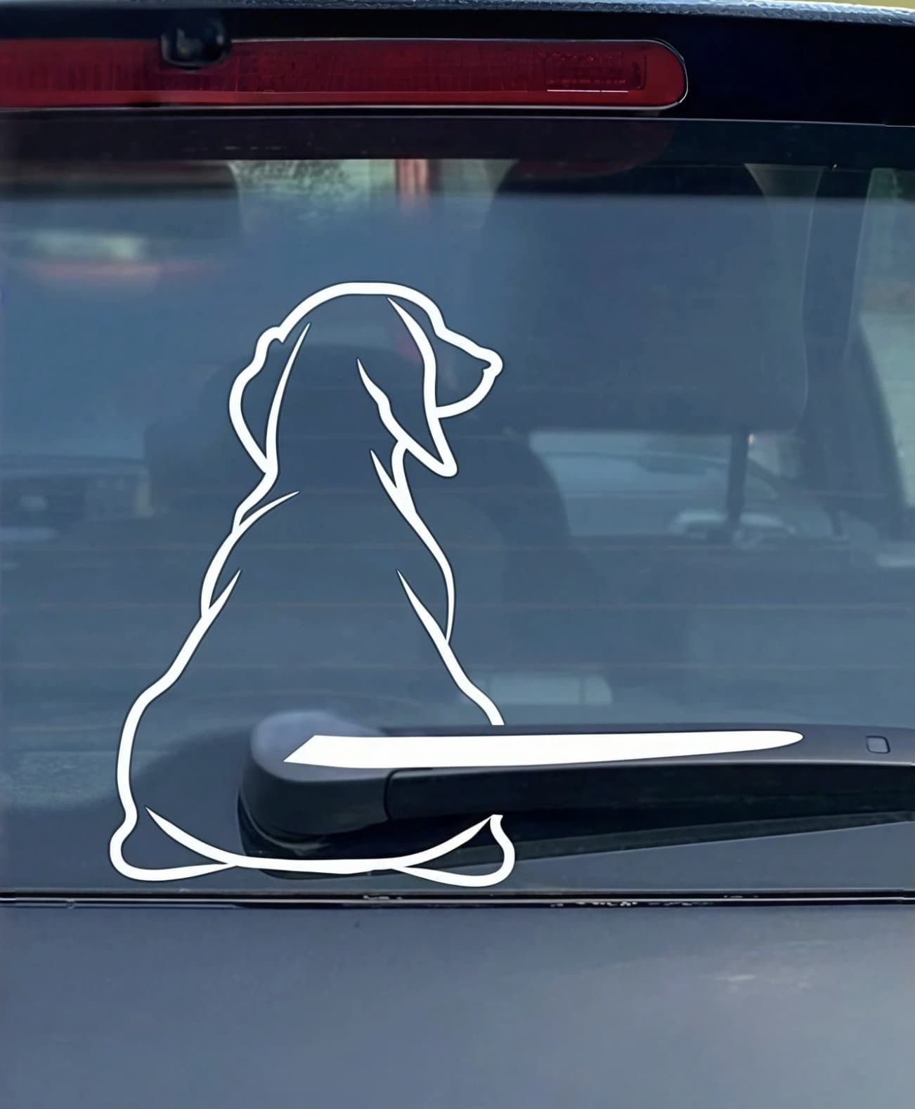 Белая наклейка силуэта сидящей собаки на заднем стекле машины