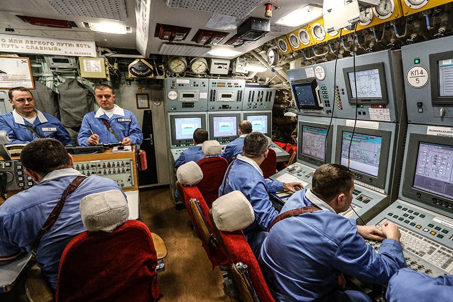 Центральный пост управления подводной лодки. Офицеры следят за показаниями приборов и картами при красном освещении.