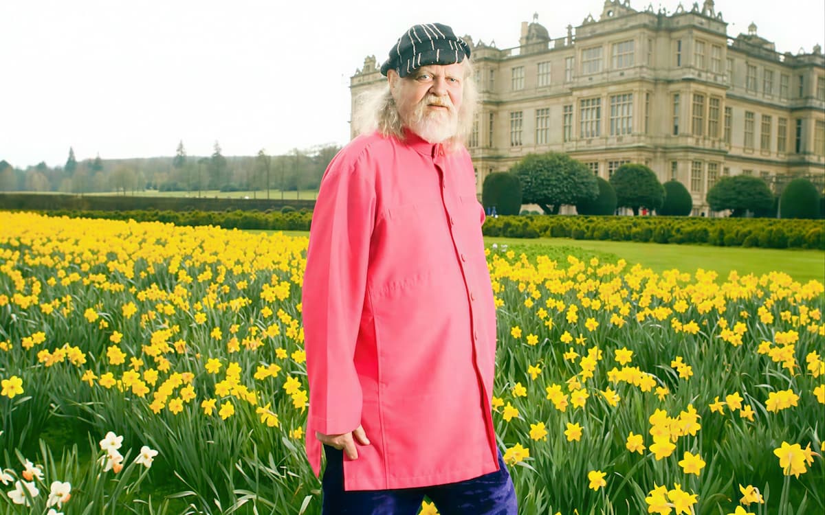 Пожилой маркиз Батский в яркой цветной рубашке стоит на фоне цветущего сада и стен Лонглита