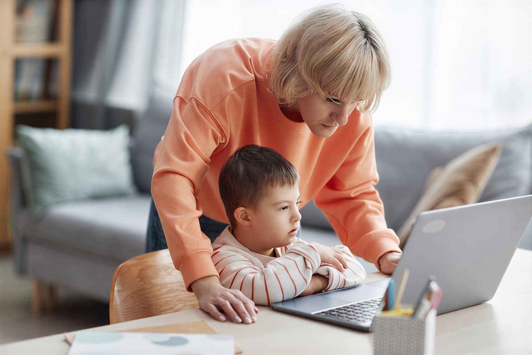 little boy with down syndrome using computer with mom assisting 1