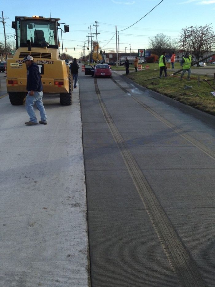 Рабочие укладывают свежий бетон, желтый погрузчик стоит на дороге