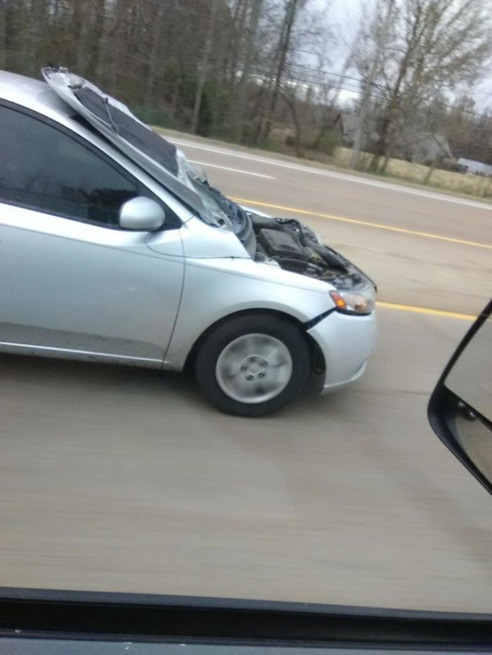 Серебристый минивэн с полностью открытым капотом едет по шоссе