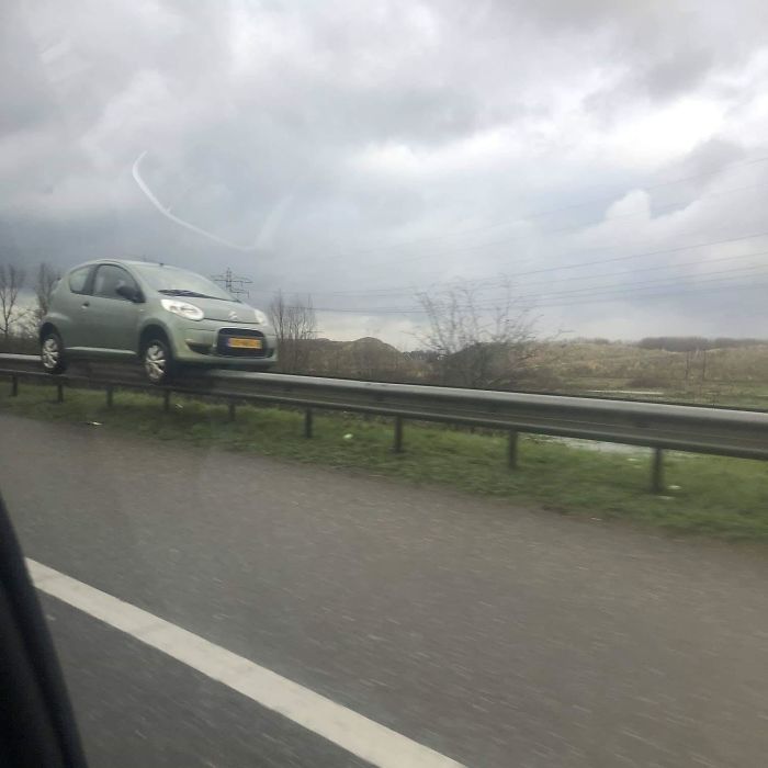 Маленький зеленый автомобиль балансирует на ограждении трассы