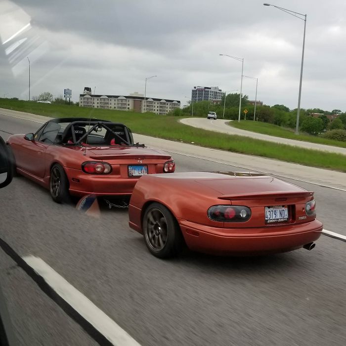 Красный родстер Mazda с прицепом в виде его же бампера на трассе