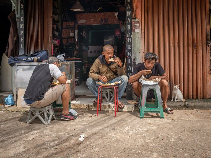 Трое мужчин едят на табуретах и белый кот у стены в Азии