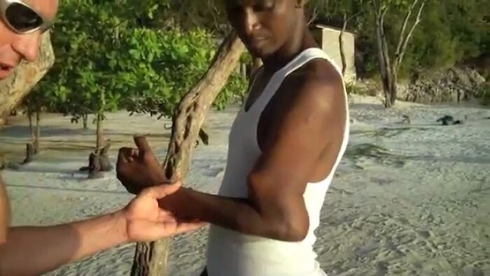 Мужчина в белой майке показывает руку на пляже