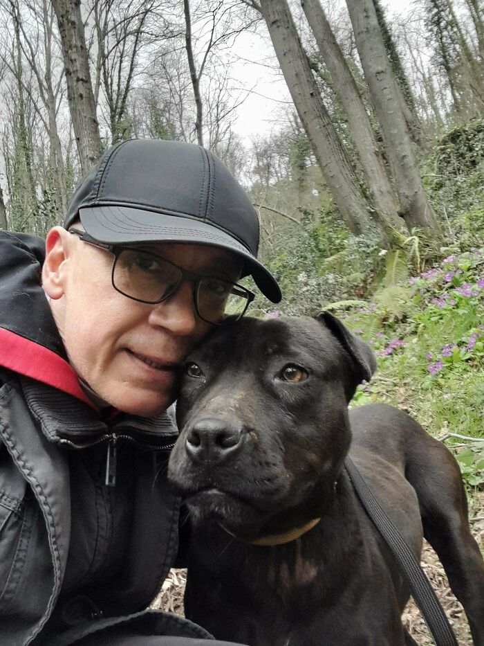 Мужчина в чёрной кепке обнимает чёрного пса в лесу