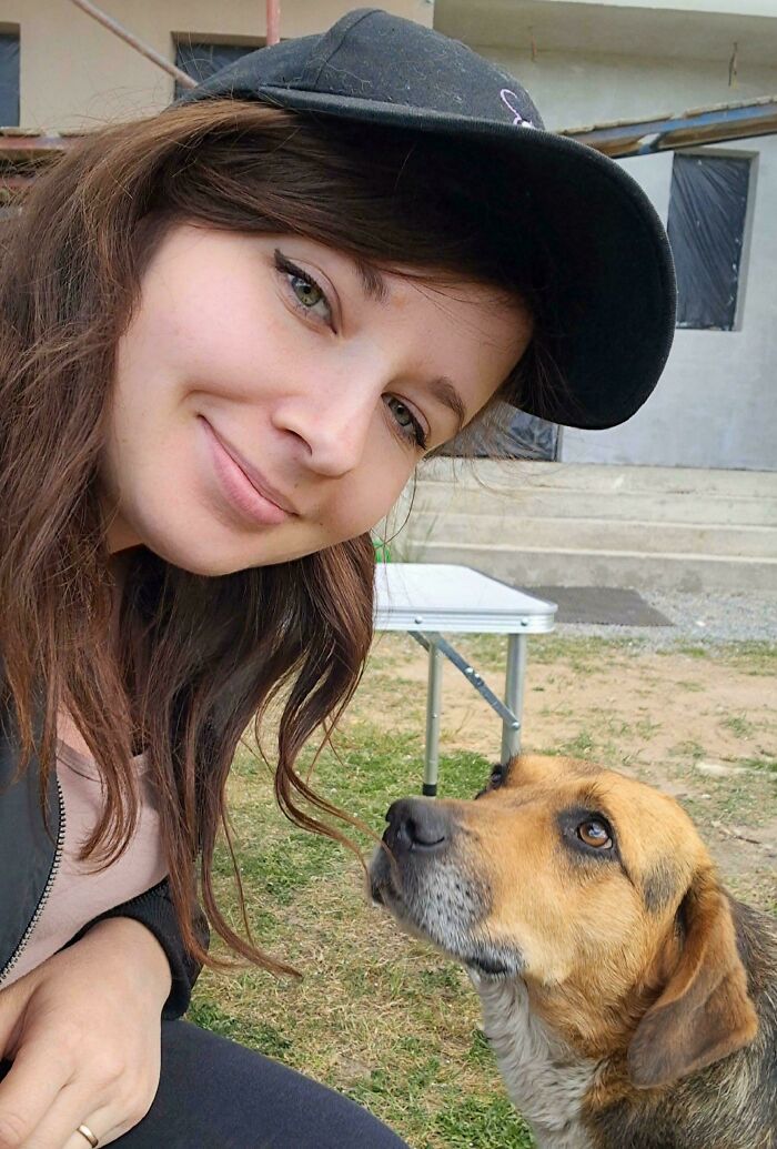 Девушка в чёрной кепке улыбается рядом с собакой на траве
