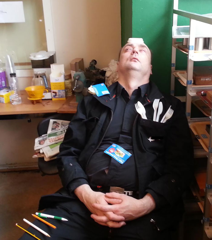 Мужчина спит сидя в офисе с вилками в кармане и бумажкой на лбу