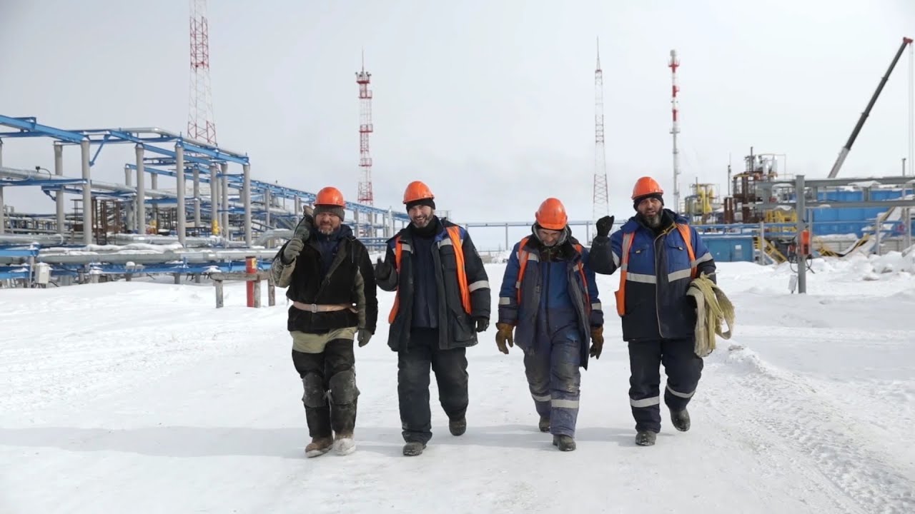 Работники нефтяного месторождения в оранжевой спецодежде и касках у производственных объектов Арктики