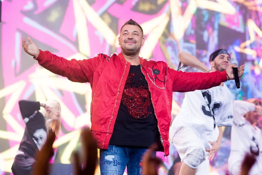 Сергей Жуков на сцене с микрофоном в энергичной позе во время выступления Руки Вверх